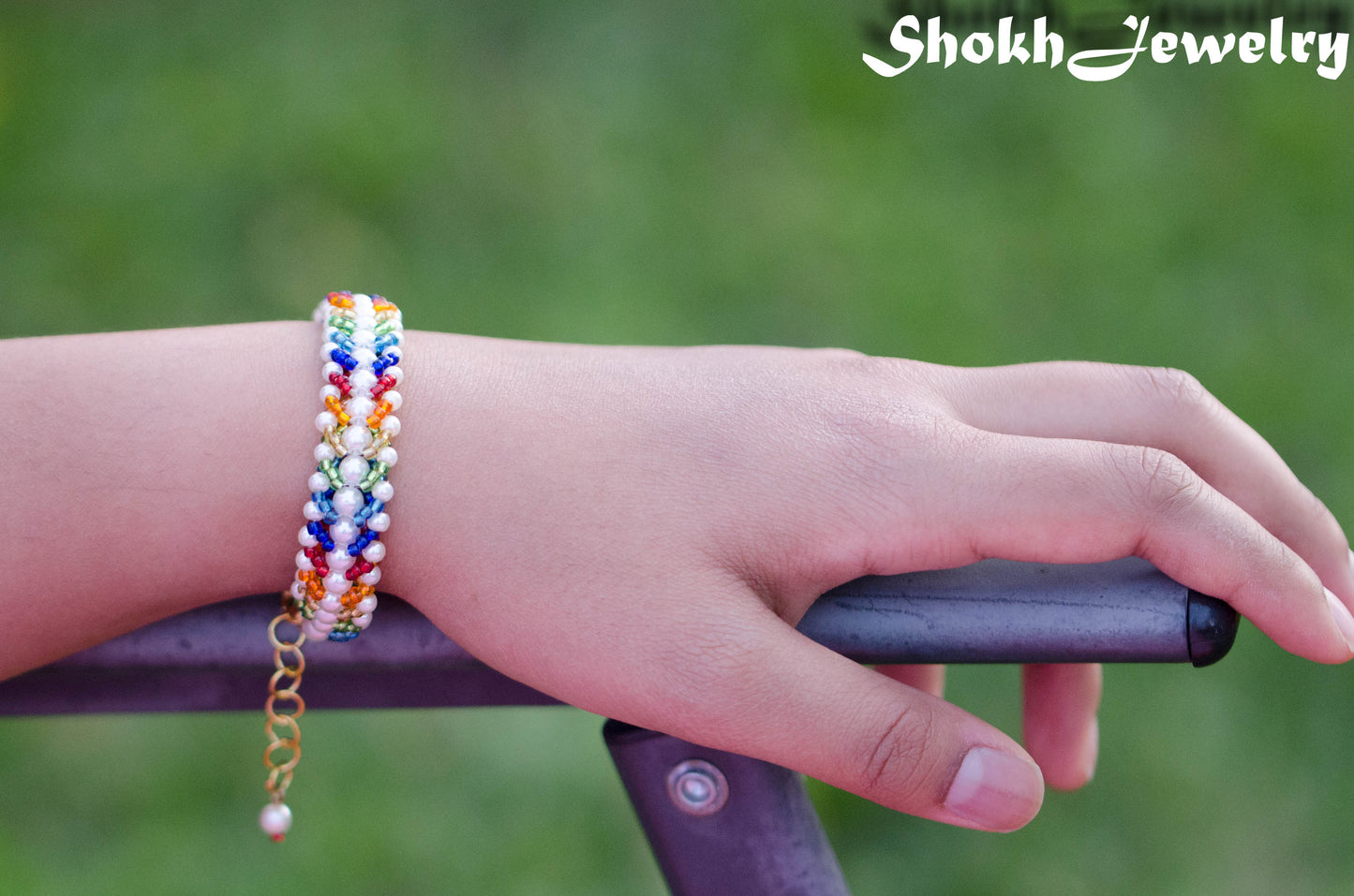 Rainbow seed bead and pearl woven bracelet on a wrist.
