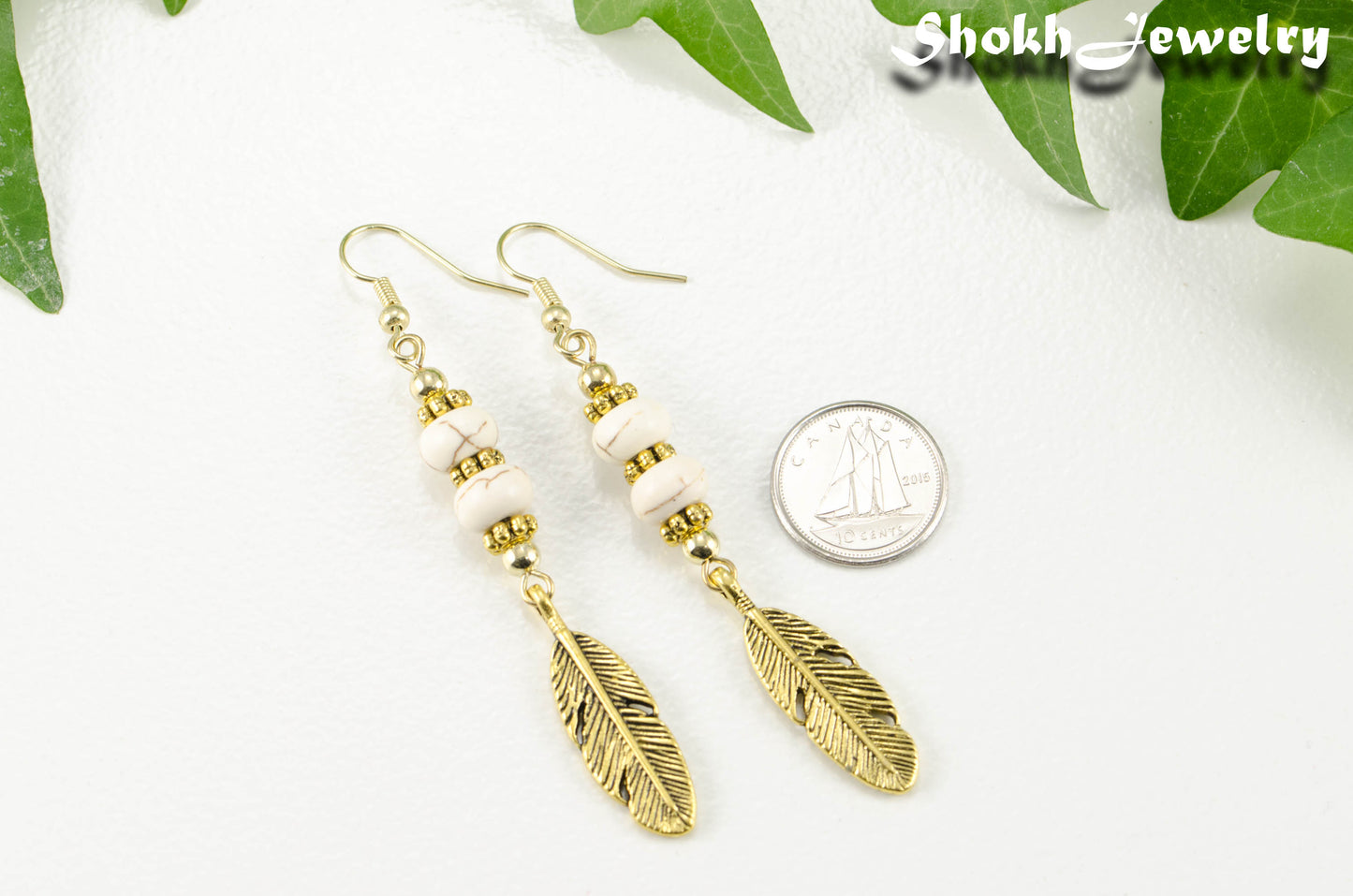 Statement White Howlite And Gold Feather Earrings beside a dime.
