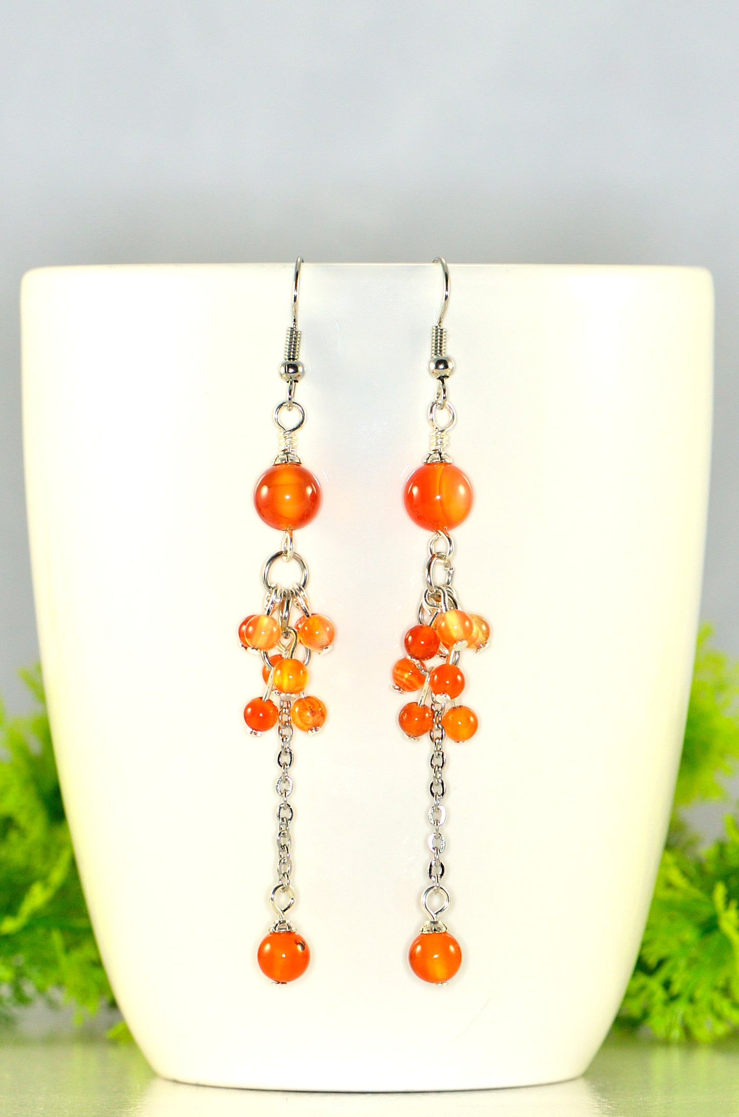 Orange carnelian beaded earrings on a white coffee mug with greenery in the background