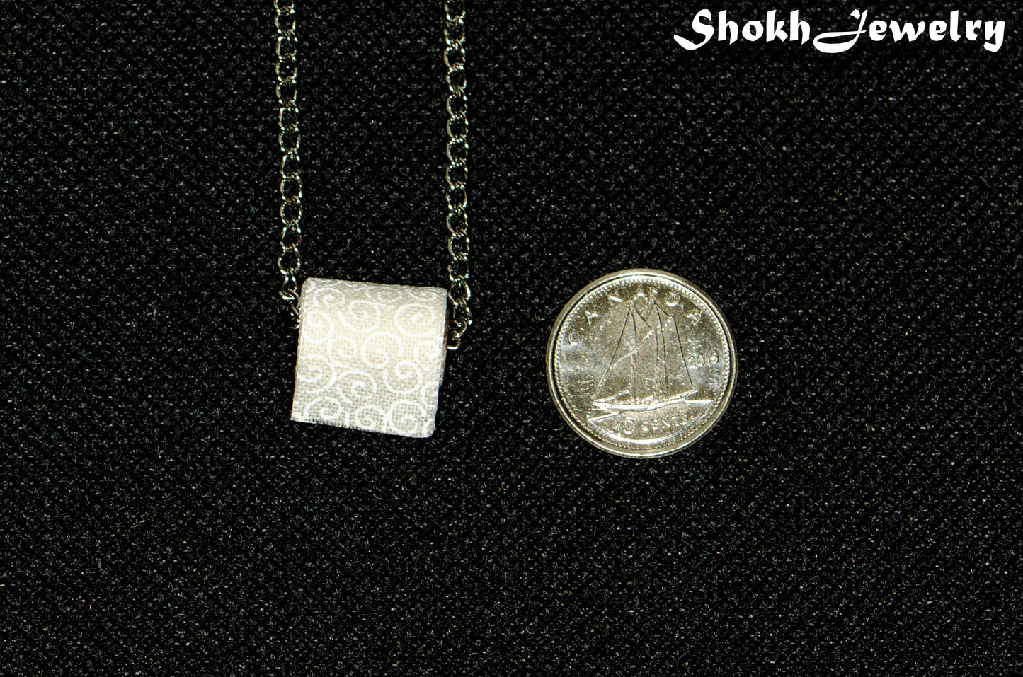 Tiny Toilet Paper Roll Necklace beside a dime.