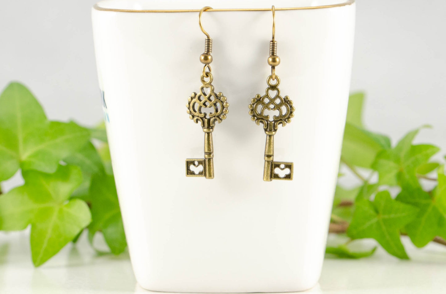 Bronze Skeleton Key Charm Earrings displayed on a tea cup.