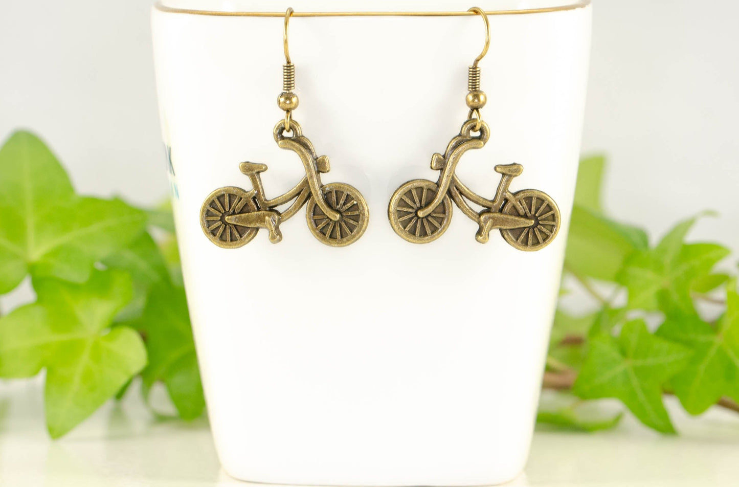 Antique Bronze Bicycle Charm Earrings displayed on a tea cup.
