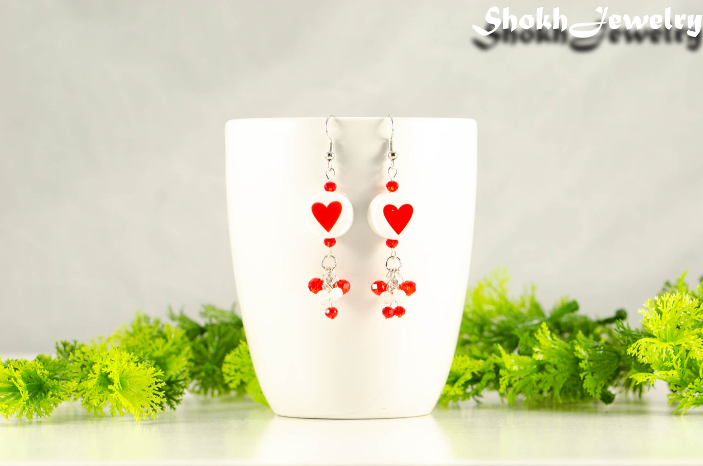 Statement Red Heart Ceramic Bead Earrings displayed on a coffee mug.