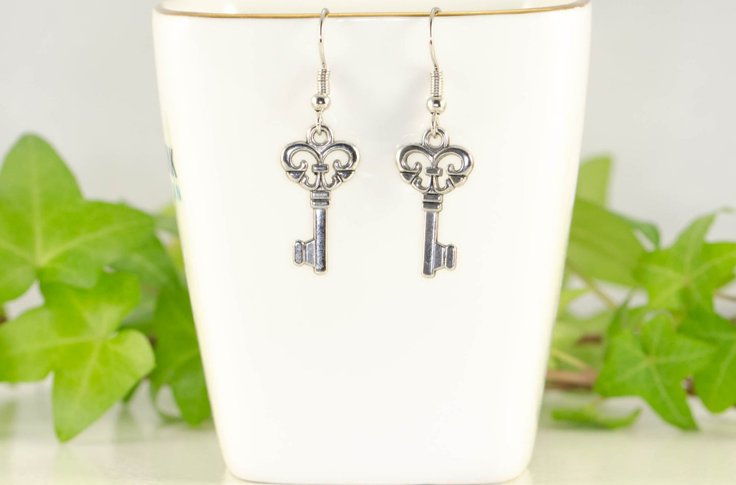 Small Skeleton Key Charm Earrings displayed on a tea cup.