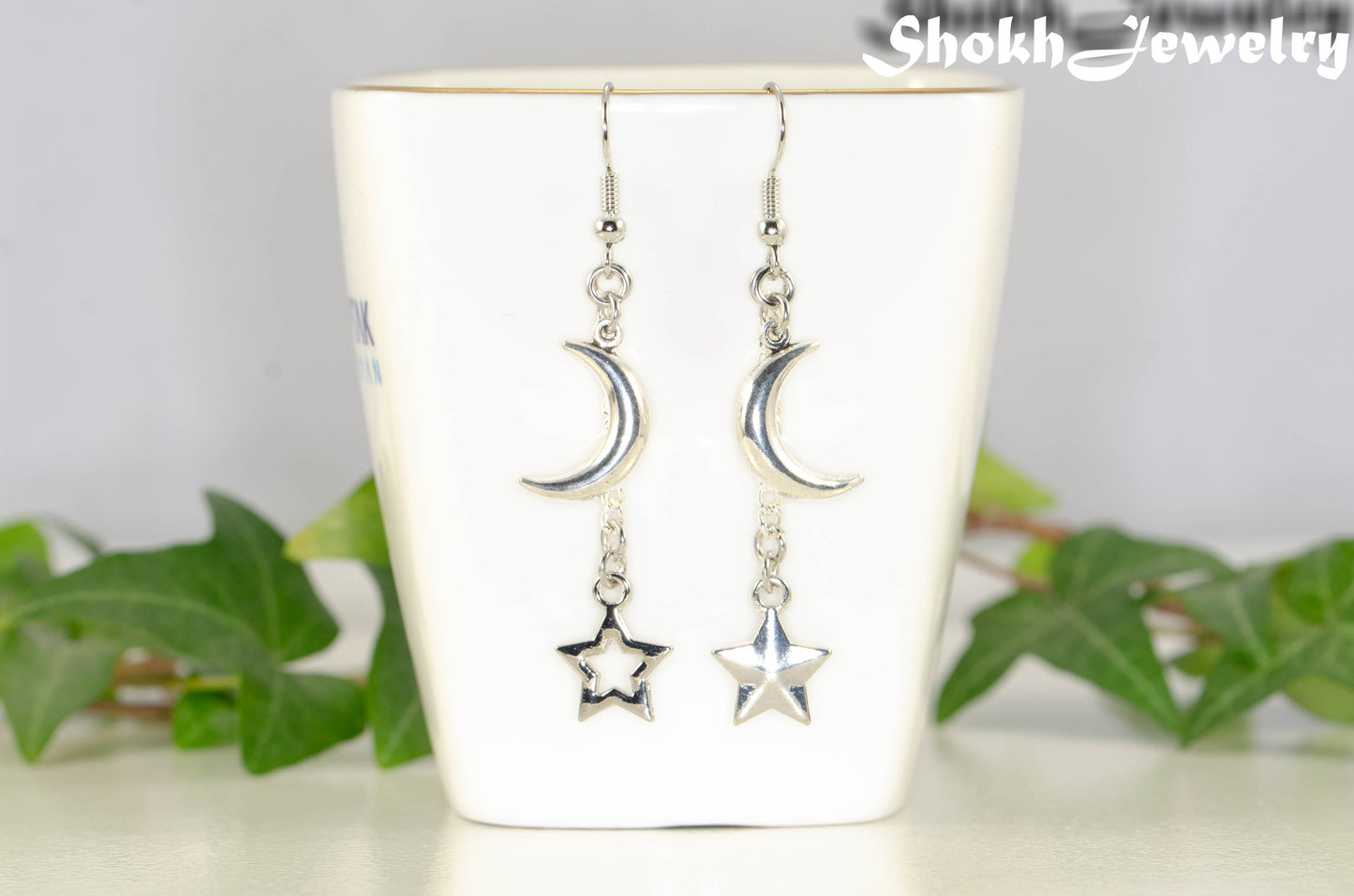 Crescent Moon and Mismatched Star Earrings displayed on a tea cup.