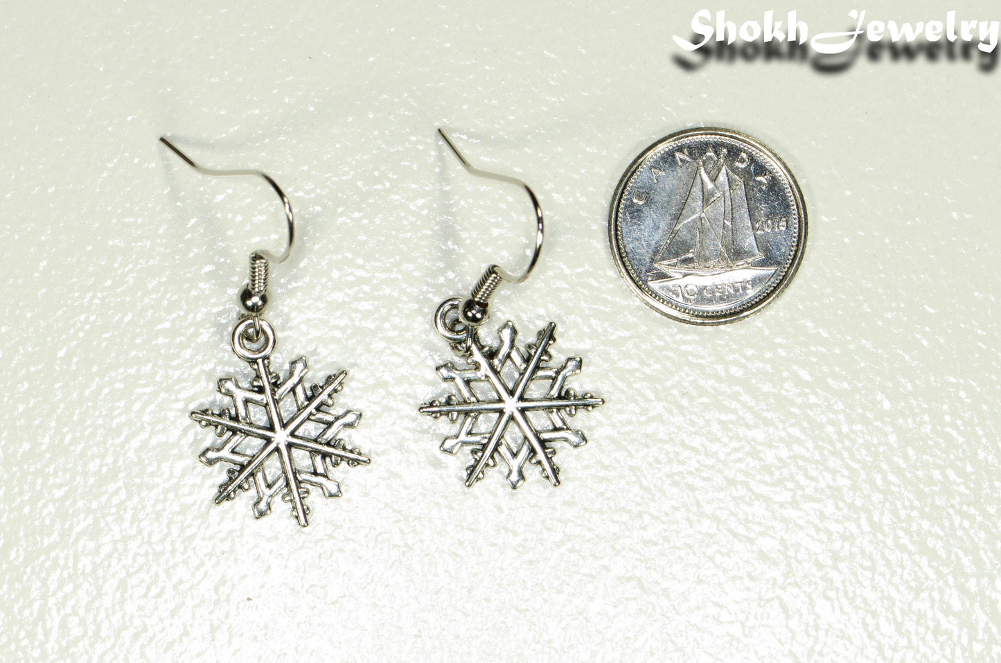 Christmas Snowflakes Charm Earrings beside a dime.
