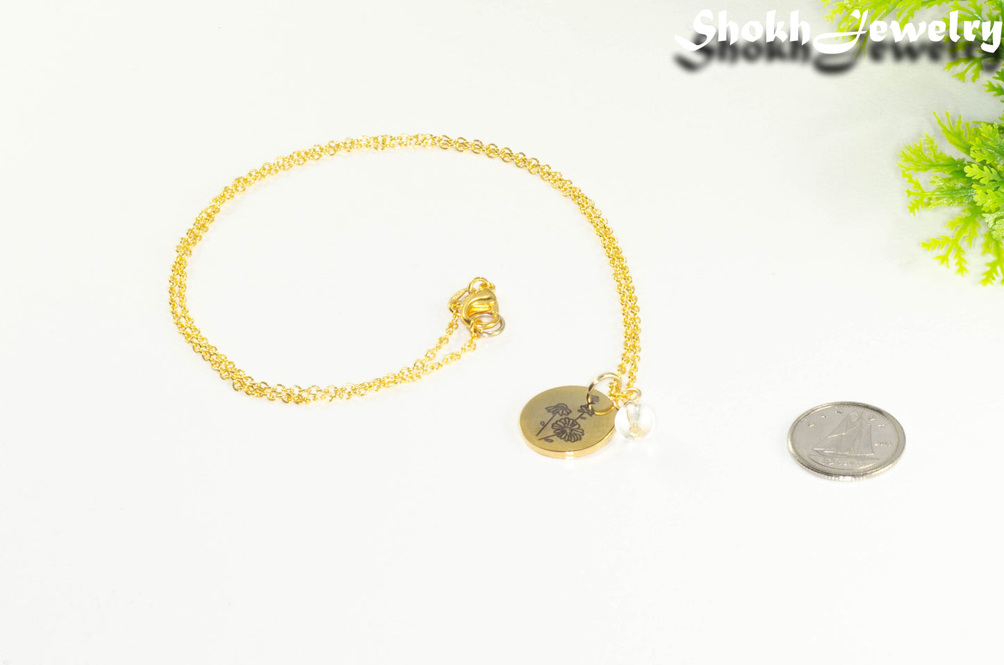 Gold Plated April Birth Flower Necklace with Clear Quartz Birthstone Pendant beside a dime.