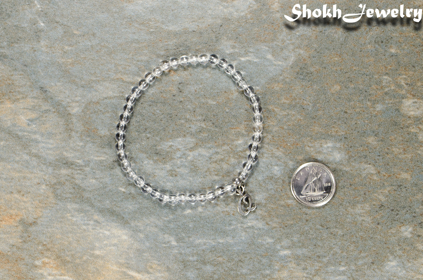 4mm Clear Quartz Bracelet with Initial beside a dime.