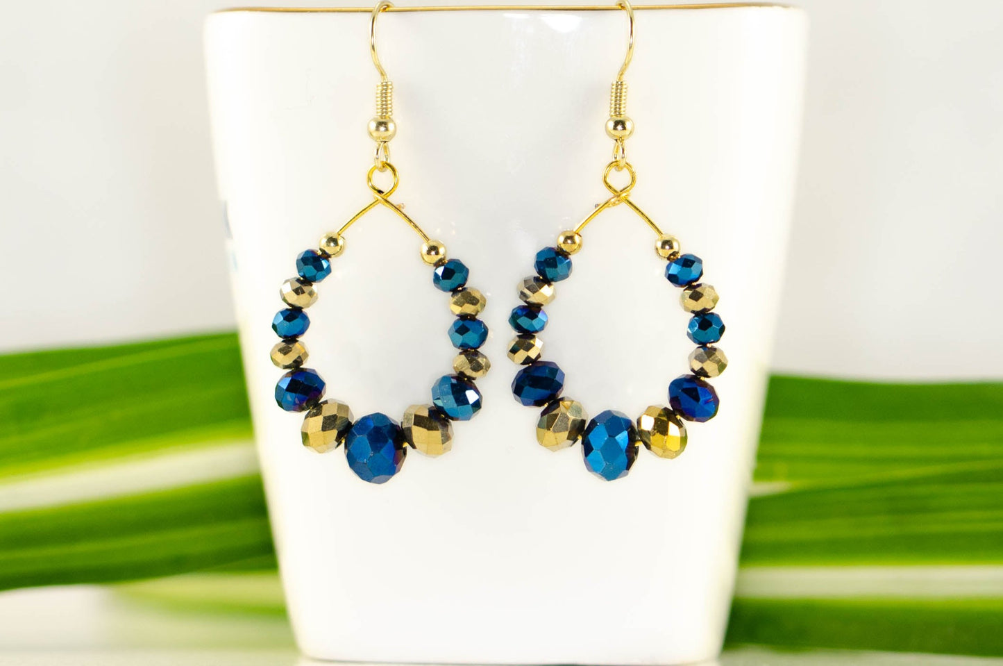Blue and Gold Glass Crystal Hoop Earrings displayed on a tea cup.