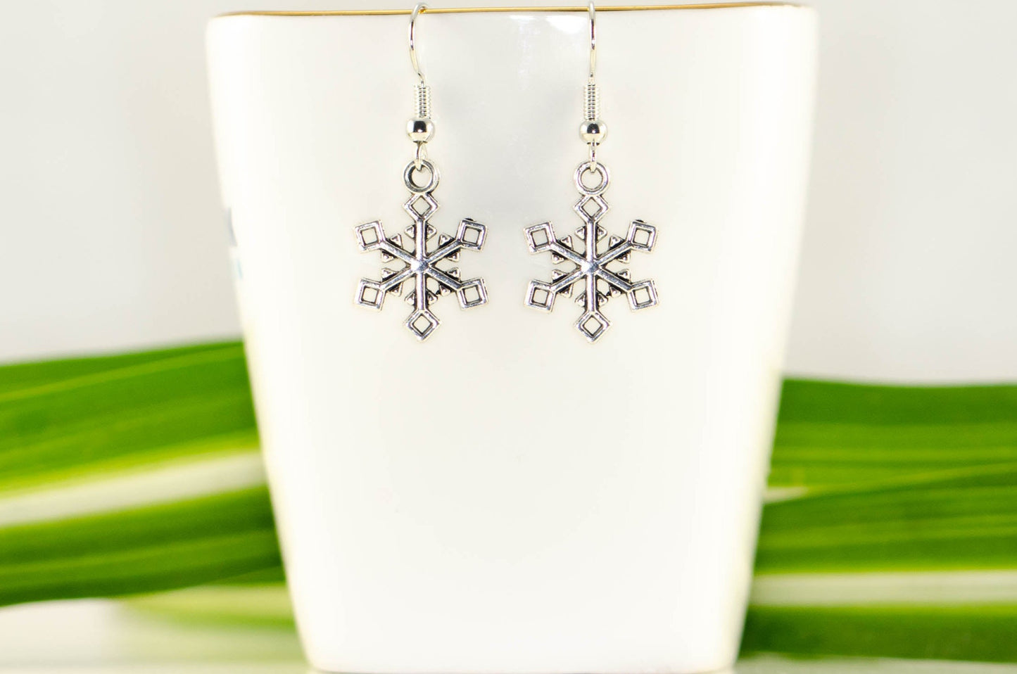 Christmas Snowflakes Charm Earrings displayed on a tea cup.