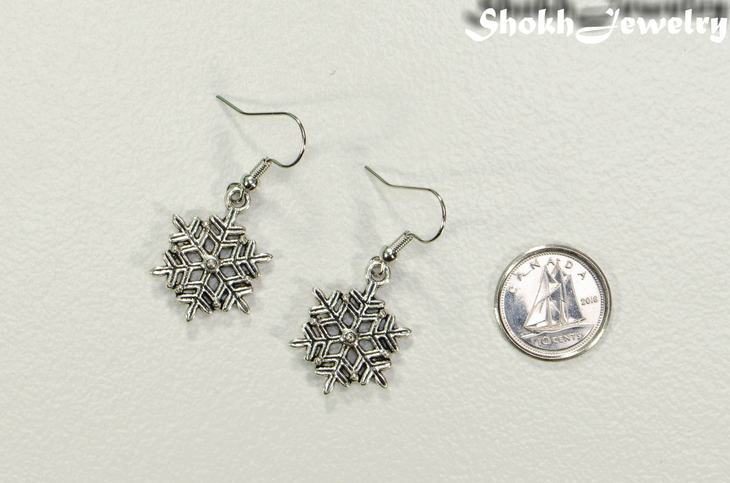 Christmas Snowflakes Charm Earrings beside a dime.