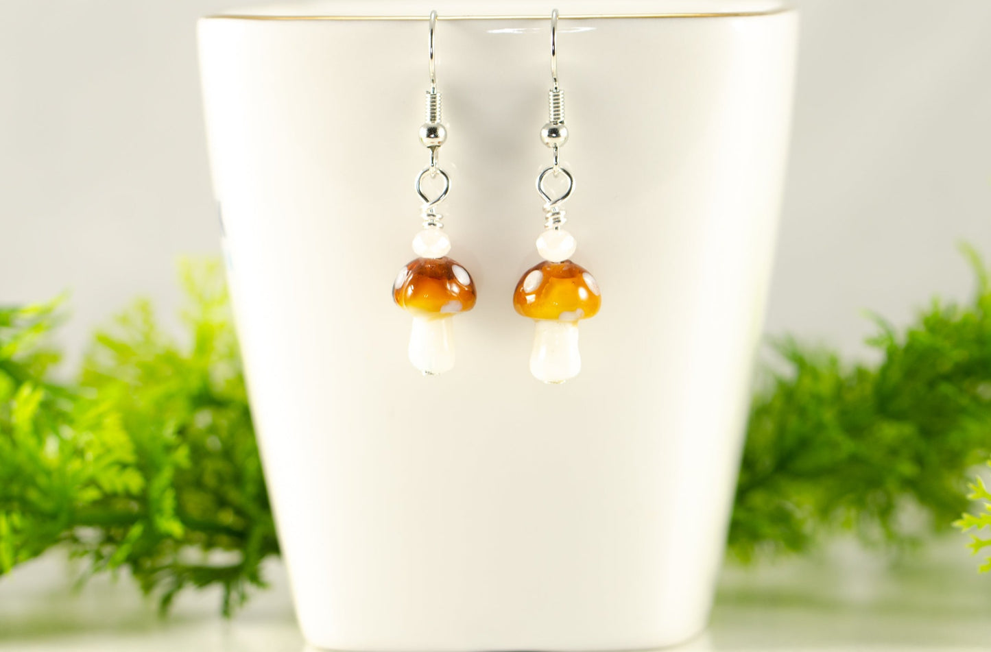 Tiny Brown Mushroom Glass Bead Earrings displayed on a tea cup.