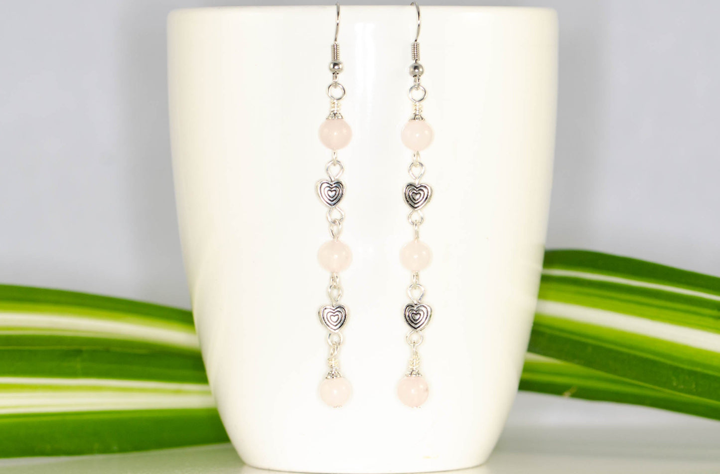 Long Rose Quartz and Heart Earrings displayed on a coffee mug.