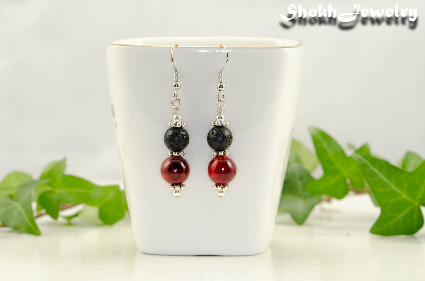 Red Quartzite and Black Lava Rock Earrings displayed on a tea cup.