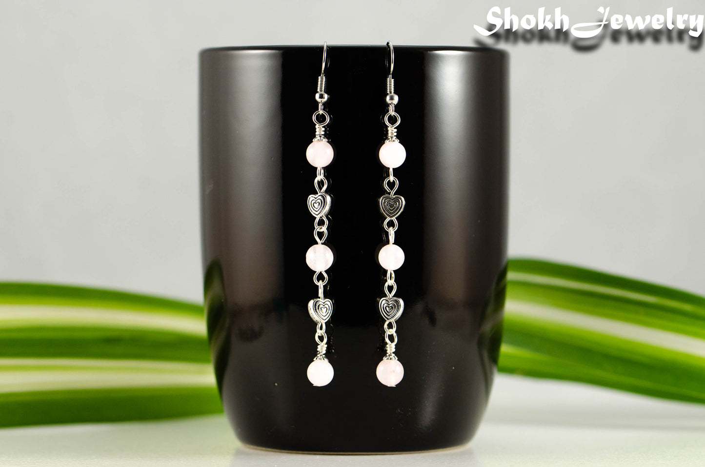 Long Rose Quartz and Heart Earrings displayed on a coffee mug.