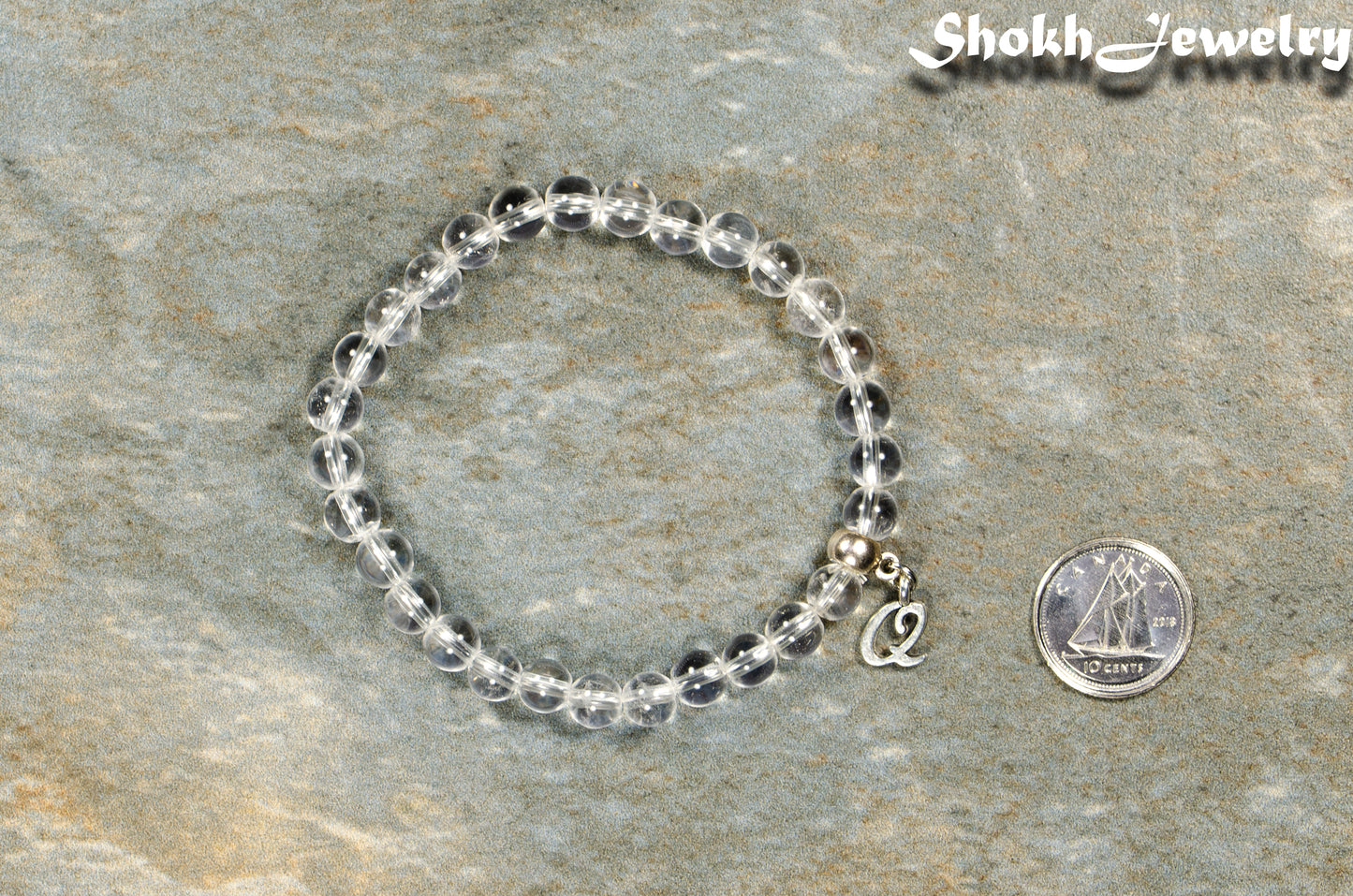6mm Clear Quartz Bracelet with Initial beside a dime.
