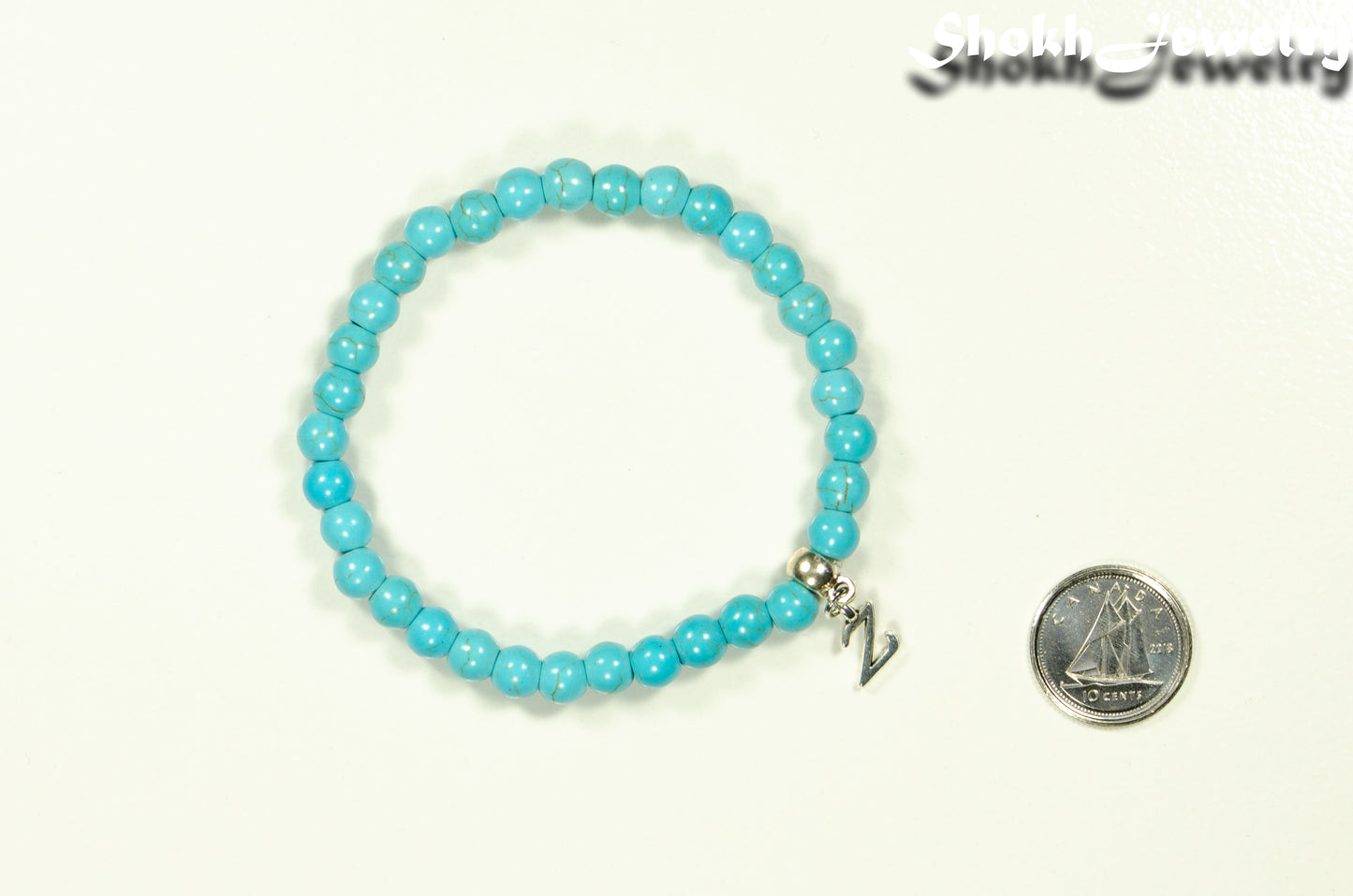 6mm Turquoise Howlite Bracelet with Initial beside a dime.
