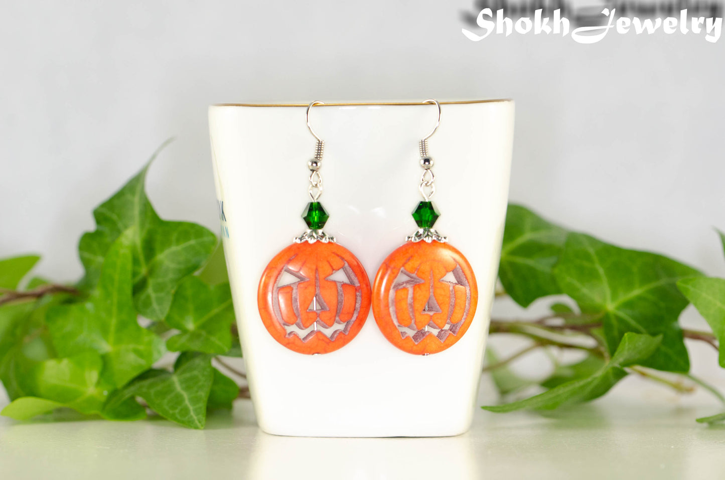 Spooky Halloween Pumpkin Earrings displayed on a tea cup.