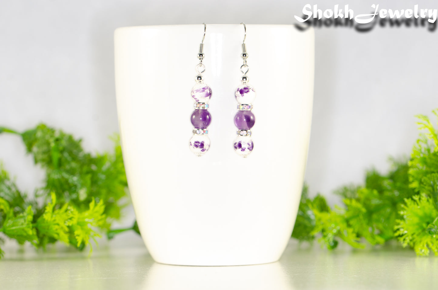 Long Floral Ceramic Bead and Amethyst Earrings displayed on a coffee mug.