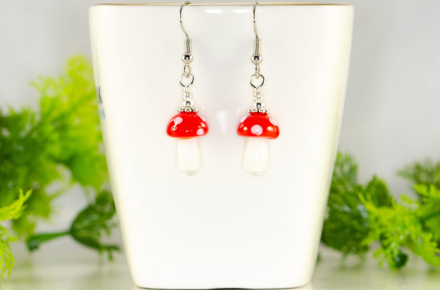 Tiny Red Mushroom Glass Bead Earrings displayed on a tea cup.