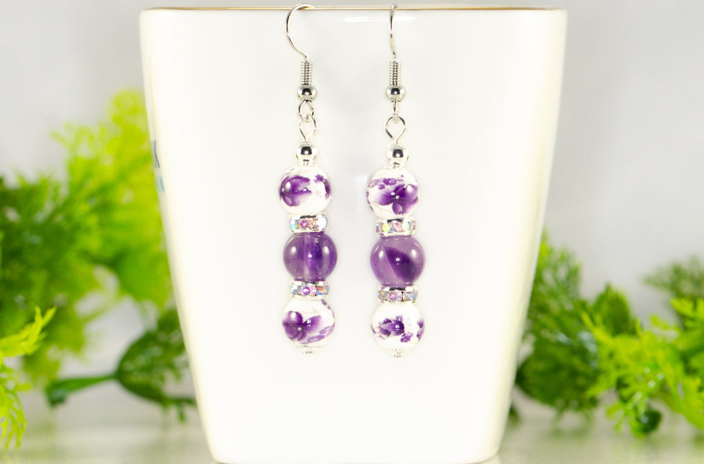 Long Floral Ceramic Bead and Amethyst Earrings displayed on a tea cup.