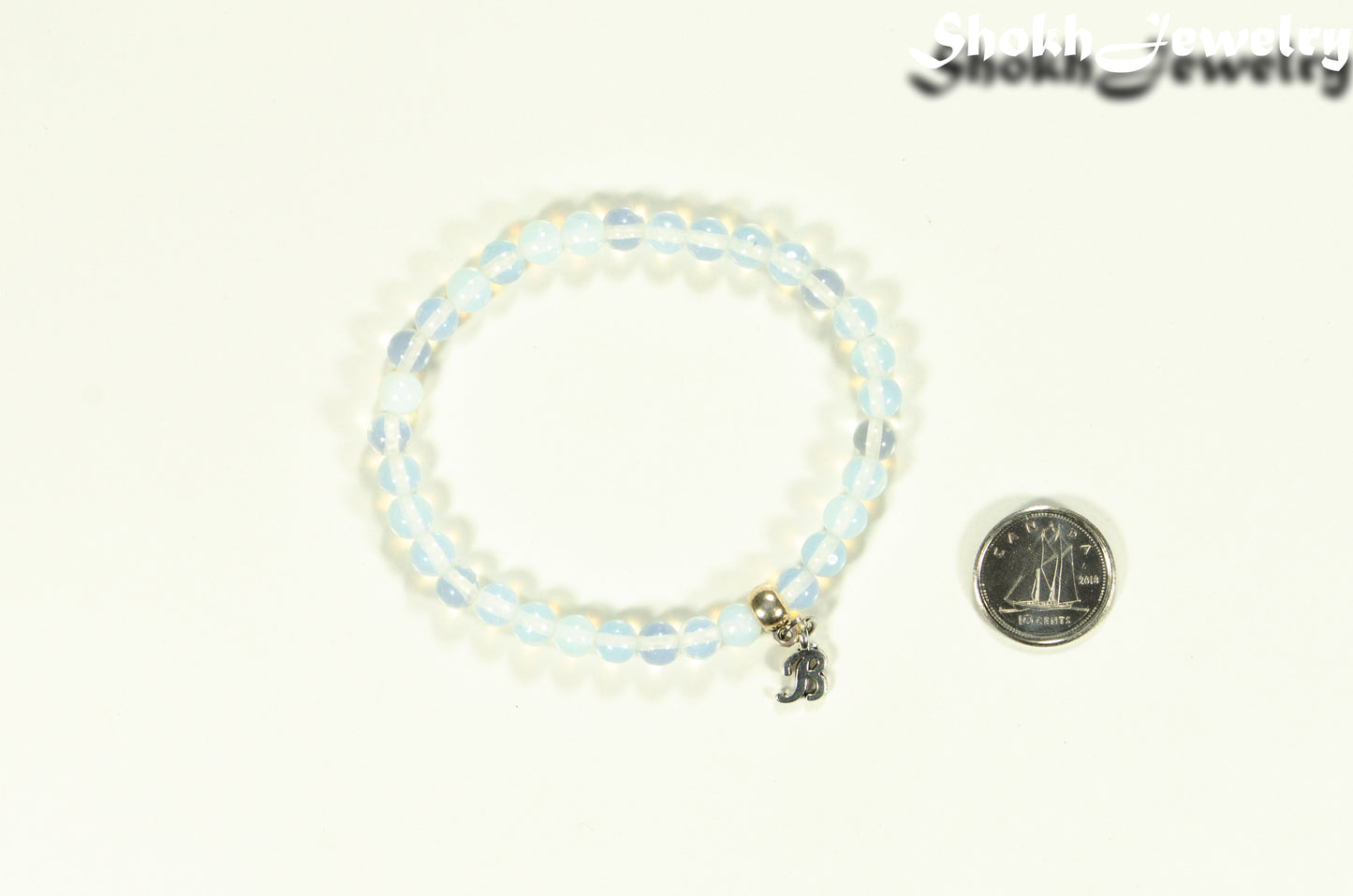 6mm White Opal Bracelet with Initial beside a dime.