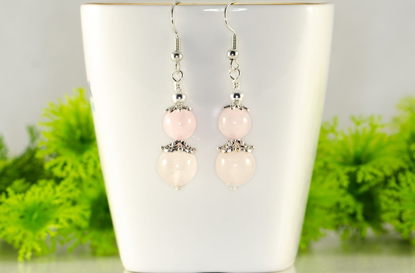 Natural Rose Quartz Crystal Dangle Earrings displayed on a tea cup.