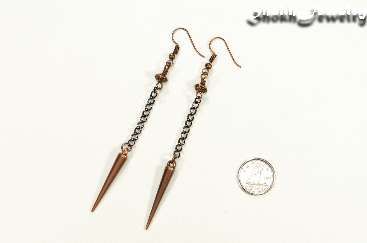Statement chain and antique copper spike earrings beside a dime