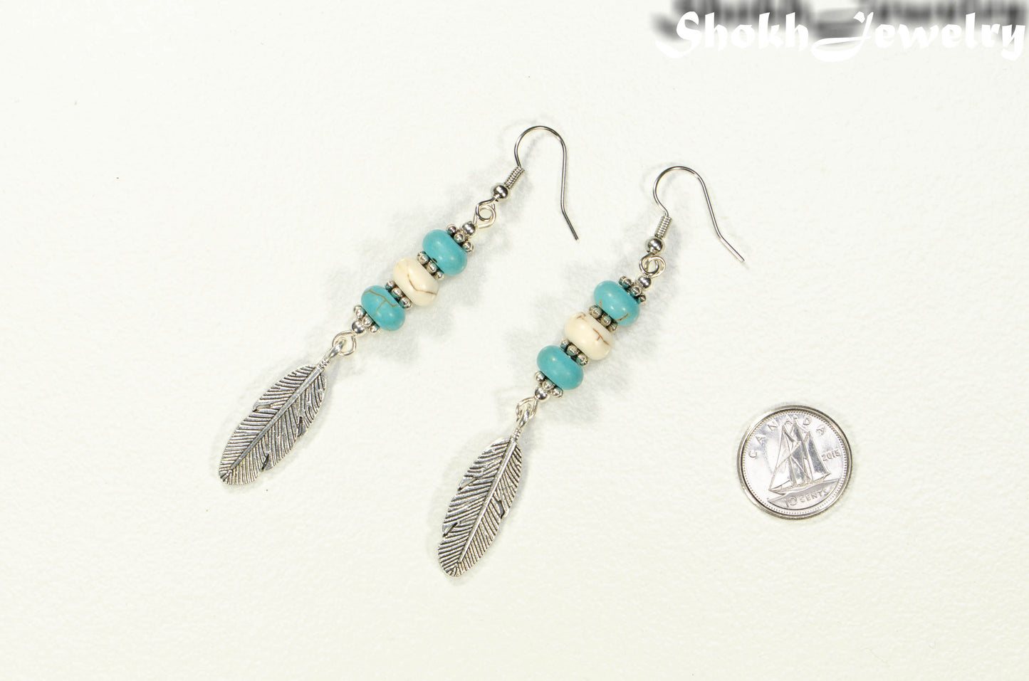 Statement Turquoise And White Howlite And Feather Earrings beside a dime.