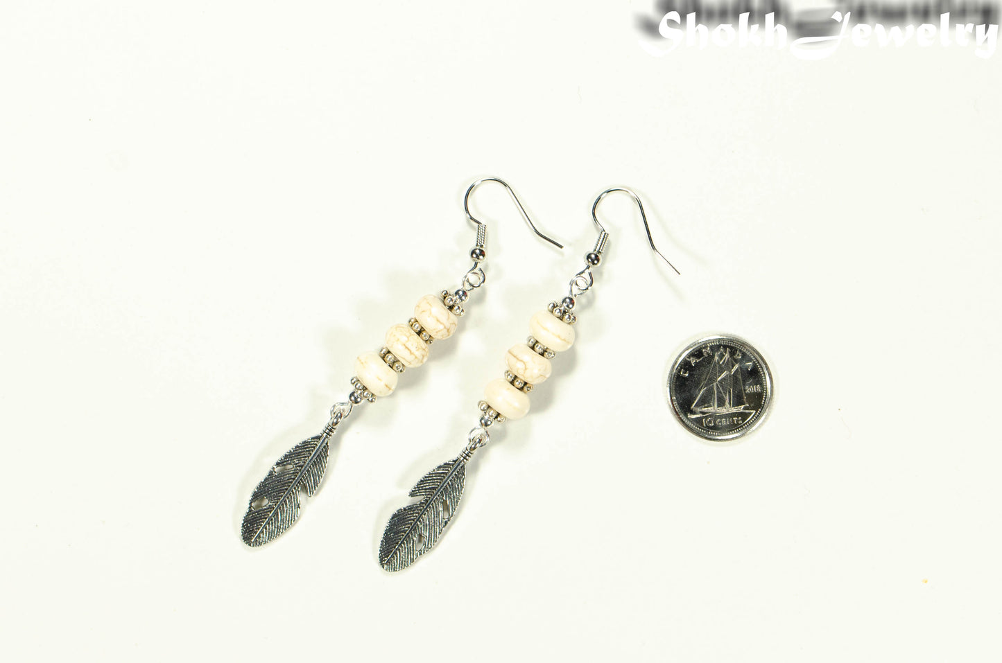 Statement White Howlite And Tibetan Silver Feather Earrings beside a dime