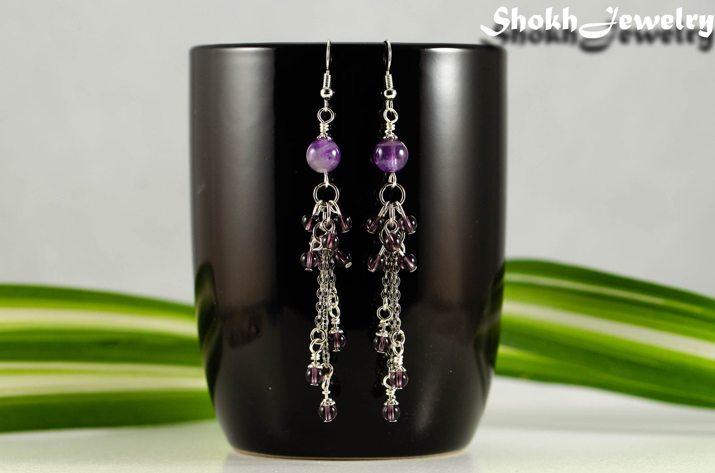 Long Stainless Steel Chain and Amethyst Earrings displayed on a black coffee mug.
