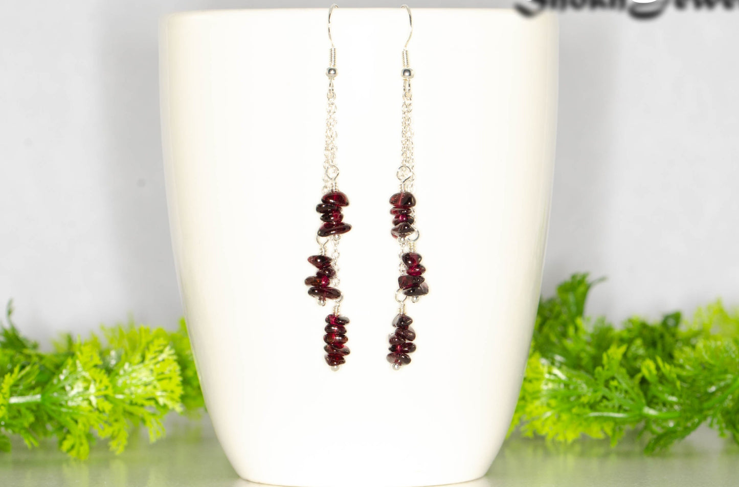 Long Silver Plated Chain and Garnet Crystal Chip Earrings on a coffee mug.