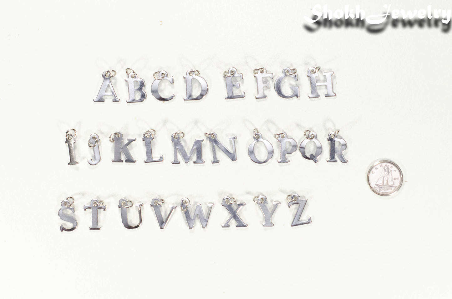 Alphabet charms beside a dime.