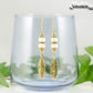 Statement White Howlite And Gold Feather Earrings displayed on a glass.