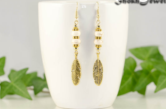 Statement White Howlite And Gold Feather Earrings displayed on a coffee mug.