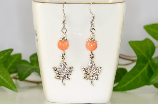 Orange Quartzite and Tibetan Silver Maple Leaf Dangle Earrings displayed on a tea cup.