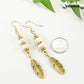 Statement White Howlite And Gold Feather Earrings beside a dime.