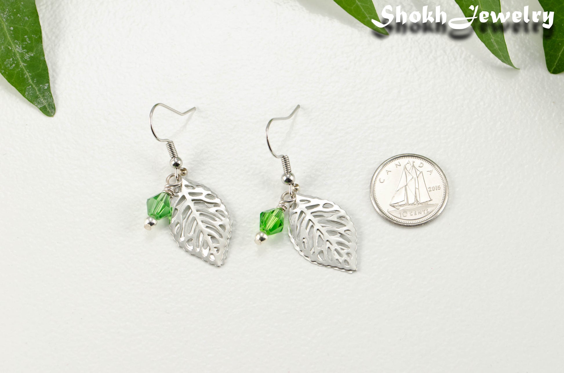 Filigree Silver Leaf Charm and Green Glass Crystal Earrings beside a dime.