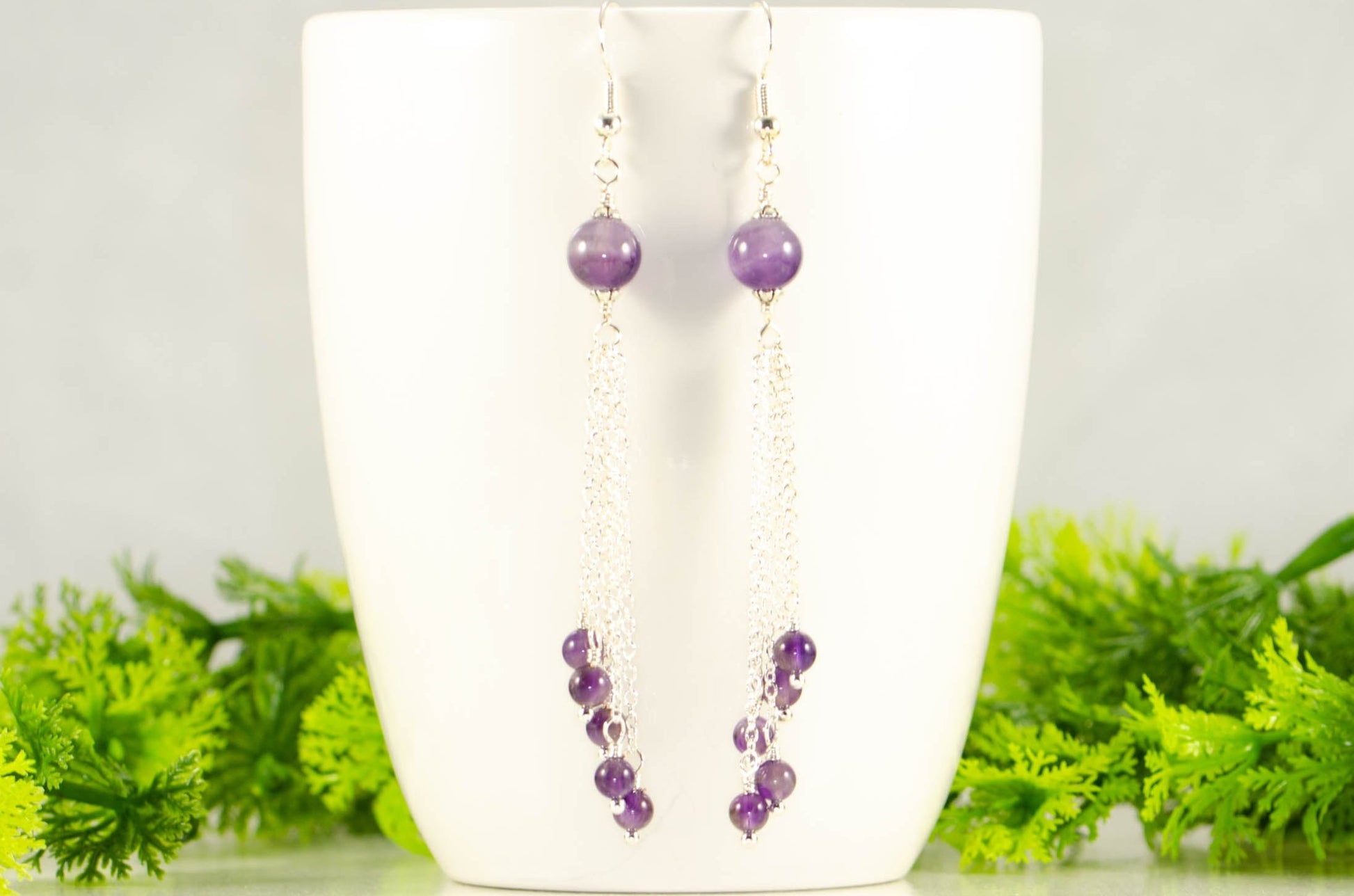 Cascading Amethyst Crystal Drop Earrings displayed on a coffee mug.