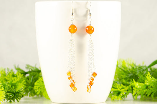 Cascading Carnelian Crystal Drop Earrings displayed on a coffee mug.