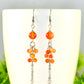 Orange carnelian beaded earrings on a white coffee mug with greenery in the background