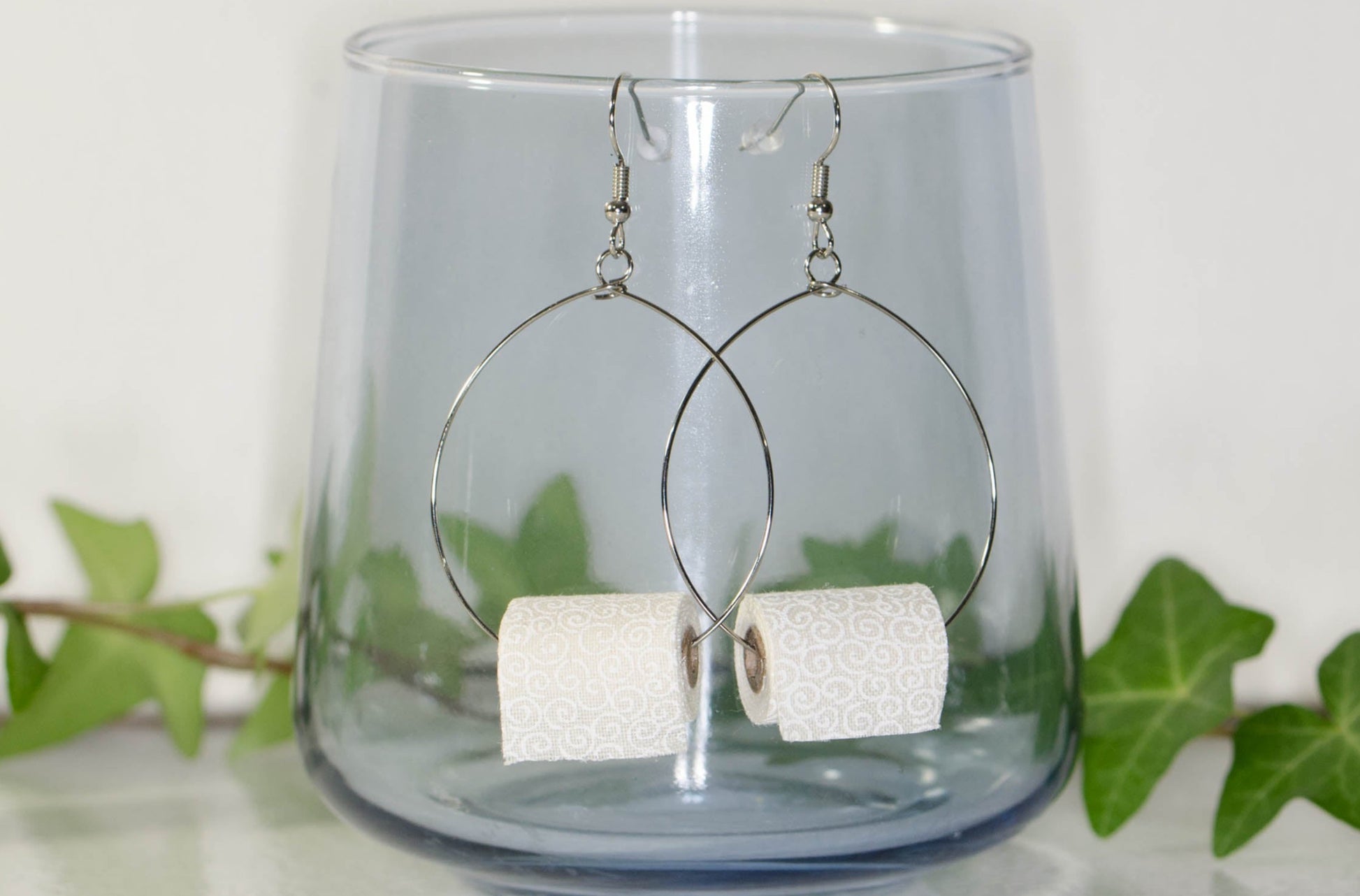 Large Miniature Toilet Paper Roll Earrings displayed on a glass.