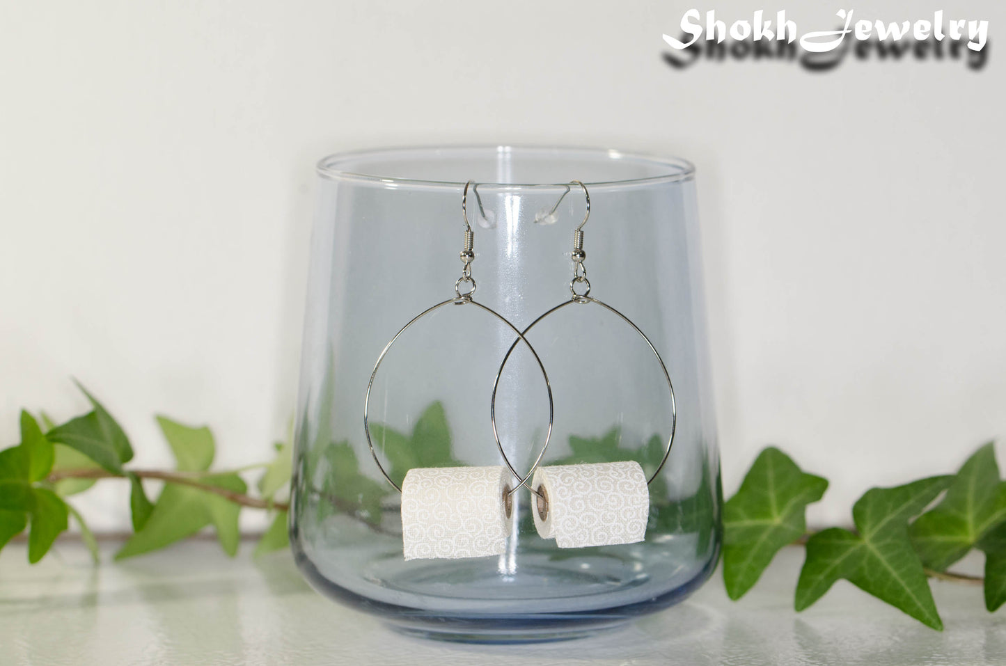 Miniature Toilet Paper Roll Earrings displayed on a glass.