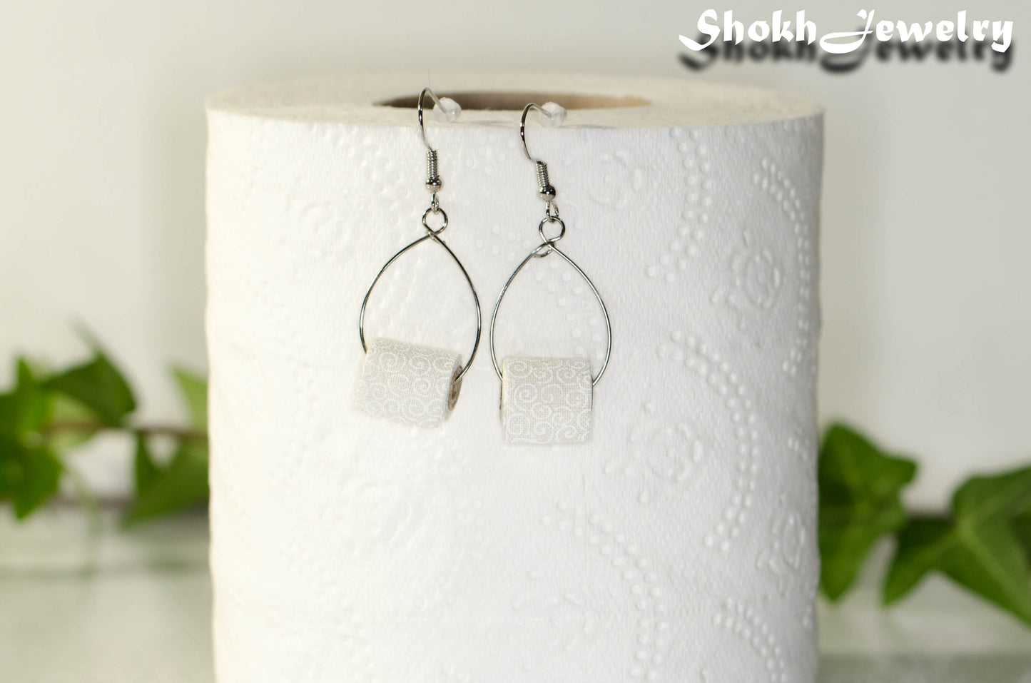 Miniature Toilet Paper Roll Earrings displayed on a toilet paper roll.