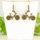 Antique Bronze Bicycle Charm Earrings displayed on a tea cup.