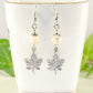 White Howlite and Tibetan Silver Maple Leaf Dangle Earrings displayed on a tea cup.
