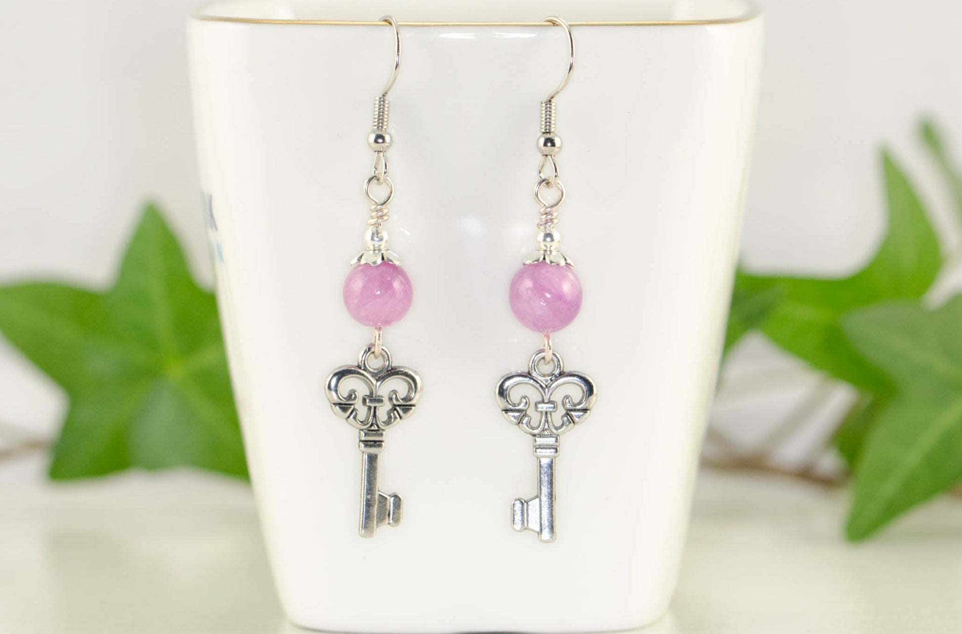 Light Purple Quartzite and Key Charm Dangle Earrings displayed on a tea cup.