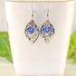 Filigree Silver Leaf Charm and Blue Glass Crystal Earrings displayed on a tea cup.