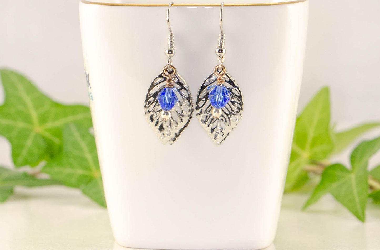 Filigree Silver Leaf Charm and Blue Glass Crystal Earrings displayed on a tea cup.