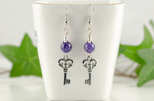 Purple Agate and Key Charm Dangle Earrings displayed on a tea cup.